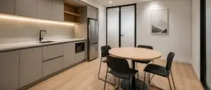 Modern office kitchenette and breakout area with grey cabinetry, timber flooring, round dining table, black chairs and minimalist neutral finishes